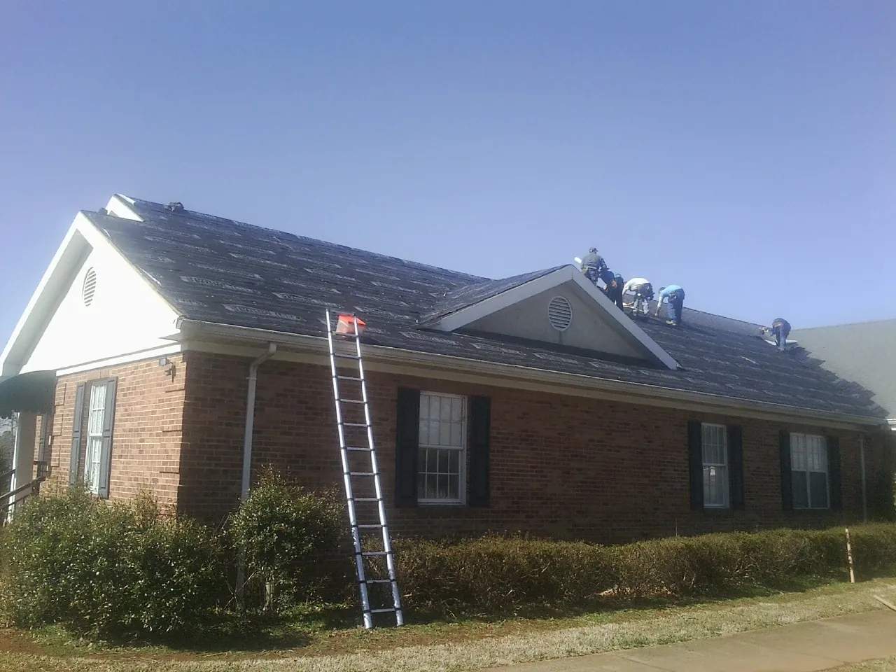 Crew tearing shingles off a brick ranch roof with a ladder set — Metal Roof Repair work by our crew in Republic